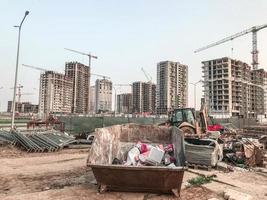 industrieel plaats. bouw van een groot woon- complex. in de centrum is een groot, roestig metaal houder voor verzamelen omvangrijk afval. De volgende naar bouw uitrusting foto