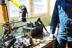 een mannetje werken elektricien in een gewaad professioneel werken Aan een tafel voor reparatie in een werkplaats voor op afstand elektronica en fabricage onderdelen en Reserve onderdelen foto