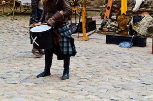 een Schots strijder, soldaat, musicus in traditioneel kostuum met een rok beats de trommel Aan de plein van een middeleeuws oud kasteel. foto