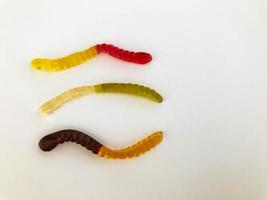 kleverig wormen van verschillend kleuren liggen Aan een wit matte achtergrond. gelatineachtig zoetheid. behandelt voor kinderen en volwassenen. lang wormen, calorierijk zoet toetje foto