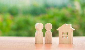 twee houten figuren van mensen en een huis Aan een natuur achtergrond. concept van betaalbaar huisvesting, hypotheken voor buying een huis voor jong gezinnen en koppels. buying en verkoop echt landgoed. familie nest foto