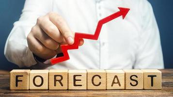 Mens houdt rood pijl omhoog over- woord voorspelling. begroting overschot, optimistisch prijs citaten, stijgen van bedrijf waarde. voorspelling verder ontwikkeling van situatie. hoog vraag naar, winstgevendheid, economisch welvaart foto