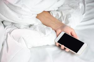 vrouw slapen in bed en Holding een smartphone in hand. foto