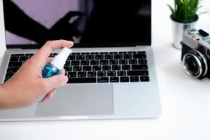 Aziatisch vrouw toepassingen een alcohol verstuiven naar schoon een laptop computer Aan haar bureau. foto