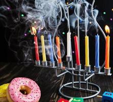 Joods vakantie Chanoeka achtergrond. een traditioneel schotel is zoet donuts. Chanoeka tafel instelling kandelaar met kaarsen en spinnen tops Aan zwart achtergrond. verlichting Chanoeka kaarsen. kopiëren ruimte foto