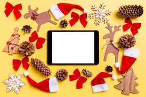 Kerstmis geel achtergrond met vakantie speelgoed en decoraties. top visie van digitaal tablet. gelukkig nieuw jaar concept foto