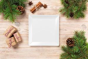 wit plein bord Aan een houten tafel. met Kerstmis decoratie, plein leeg gerecht. nieuw jaar concept foto