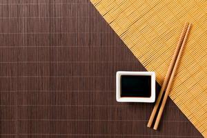 eetstokjes en kom met soja saus Aan twee bamboe mat blak en geel top visie met kopiëren ruimte foto