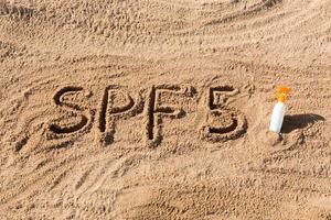 zon beschermen factor vijf. spf 5 woord geschreven Aan de zand en wit fles met zonnebrand room. huid zorg concept achtergrond foto