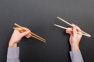 creatief beeld van houten eetstokjes in twee mannetje handen Aan zwart achtergrond. Japans en Chinese voedsel met kopiëren ruimte foto