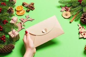 top visie van vrouw Holding een envelop Aan groen achtergrond gemaakt van vakantie decoraties. Kerstmis tijd concept foto