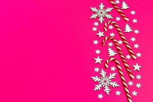 Kerstmis snoep riet gelogen gelijkmatig in rij Aan roze achtergrond met decoratief sneeuwvlok en ster. vlak leggen en top visie foto