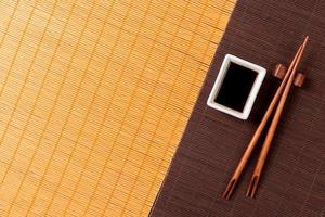 eetstokjes en kom met soja saus Aan twee bamboe mat blak en geel top visie met kopiëren ruimte foto
