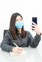 vrouw lang haar- vervelend beschermend masker Holding en gebruik makend van mobiel telefoon foto