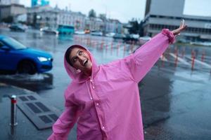 jong glimlachen vrouw in een roze regenjas genieten van een regenachtig dag. foto