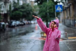 jong glimlachen vrouw met regenjas terwijl genieten van een regenachtig dag. foto