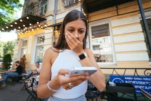mooi vrouw een stedelijk straat naar lezen een sms Aan haar mobiel telefoon foto