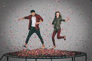 pret tijd. in de lucht schot van mooi jong vrolijk paar jumping Aan trampoline samen met confetti allemaal in de omgeving van hen foto