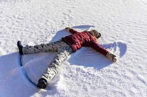 jong vrouw aan het liegen in de sneeuw en maken een sneeuw engel. winter wandelingen en pret foto