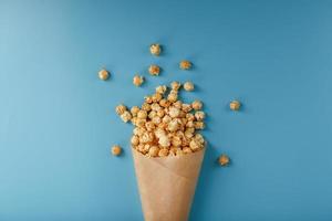 popcorn in karamel glazuur in een papier envelop Aan een blauw achtergrond. foto