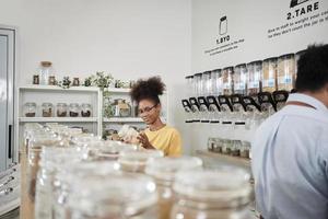 jong Afrikaanse Amerikaans vrouw is kiezen en boodschappen doen voor biologisch producten in bijvullen op te slaan met herbruikbaar container, Zero waste boodschap, en plasticvrij, milieuvriendelijk, duurzame levensstijlen. foto