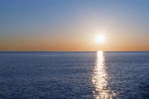 een zonnig zonsondergang Aan de zee uitrekken in de horizon met een pad en highlights Aan de zee. foto