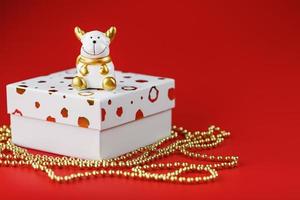nieuw jaar 2021 speelgoed- stier met een geschenk Aan een rood achtergrond. geschenk doos en goud kralen. foto