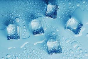 ijs kubussen met druppels van smelten water water Aan een blauw achtergrond, top visie. foto