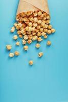 popcorn in karamel glazuur in een papier envelop Aan een blauw achtergrond. foto