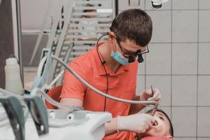 tandheelkundig behandeling van een kind, verwijdering van cariës met een oefening, Open mond en uitwerper speeksel. foto
