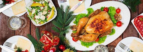 gebakken kalkoen of kip. de Kerstmis tafel is geserveerd met een kalkoen, versierd met helder klatergoud en kaarsen. gebakken kip, tafel. Kerstmis diner. vlak leggen. top visie. banier foto
