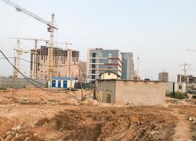 verlaten bouw plaats. in de afstand, bouw kranen zijn gebouw huizen. Daar is een veel van zand Aan de plaats, verlaten huizen zonder ramen en deuren foto