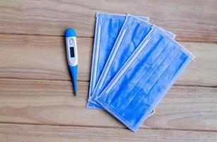 drie blauw masker, geplaatst Aan een houten tafel met een digitaal thermometer. foto