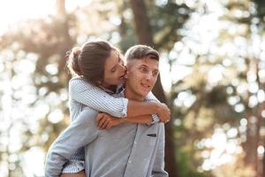 jong paar in liefde hebben plezier, lachend, meeliften in de zomer park. vrouw en Mens, vervelend in denim kleding zijn hebben datum buitenshuis. romantisch relatie. valentijnsdag dag foto