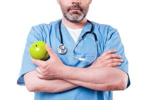 eten gezond detailopname van chirurg in blauw uniform Holding groen appel terwijl staand geïsoleerd Aan wit foto