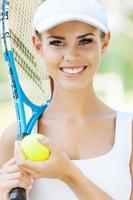 klaar naar Speel mooi jong vrouw in sport- kleding Holding tennis racket en glimlachen foto