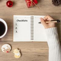 vrouw hand- schrijven checklist Aan notitieboekje met zwart koffie kop en Kerstmis koekjes Aan tafel. Kerstmis, gelukkig nieuw jaar, doelen, oplossing, naar Doen lijst, strategie en plan concept foto