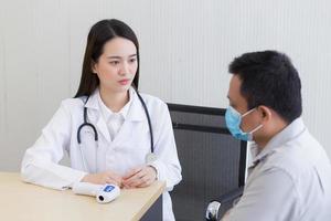 Aziatisch vrouw dokter met een wit laboratorium jas geven raad met een Mens geduldig foto