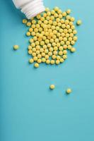 geel vitamine c capsules gemorst uit van een wit pot tegen een blauw achtergrond. foto