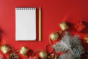 kladblok en potlood voor schrijven wensen en cadeaus voor de nieuw jaar en Kerstmis in de omgeving van de Kerstmis boom decoraties Aan een rood achtergrond. foto