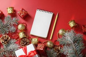 Kerstmis samenstelling met kladblok en een potlood voor schrijven wensen met Kerstmis boom decoraties Aan een rood achtergrond. foto