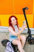 vrouw gebruikt een smartphone en een elektrische scooter in de zomer in de stad foto
