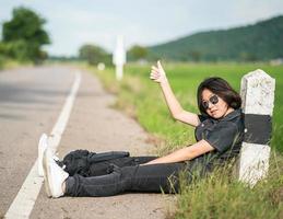 vrouw zitten met rugzak liften langs een weg in platteland foto