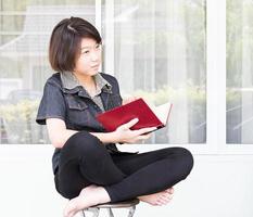 jong vrouw lezing boek zittend Aan stoel foto