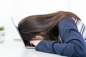 jonge vrouw lang haar valt in slaap op bureau met laptop foto