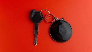 zwart motorfiets sleutel met zwart ronde sleutelhanger Aan rood achtergrond. sleutelhanger mockup voor ontwerp foto