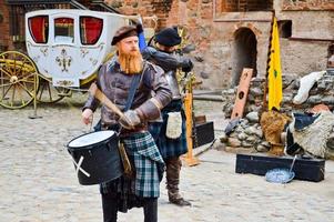 een Schots strijder, soldaat, musicus met een rood baard in traditioneel kostuum met een rok beats de trommel Aan de plein van een middeleeuws oud kasteel. nesvizh, Wit-Rusland, oktober 12, 2018 foto