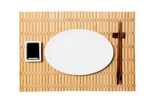 leeg ovaal wit bord met eetstokjes voor sushi en soja saus Aan geel bamboe mat achtergrond. top visie met kopiëren ruimte voor u ontwerp foto