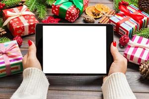 top visie van vrouw handen Holding een tablet Aan houten Kerstmis achtergrond gemaakt van Spar boom en feestelijk decoraties. nieuw jaar vakantie concept. mockup foto