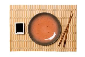 leeg ronde bruin bord met eetstokjes voor sushi en soja saus Aan geel bamboe mat achtergrond. top visie met kopiëren ruimte voor u ontwerp foto
